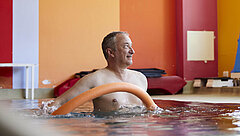 Ein Mann steht mit einer Poolnudel in einem Schwimmbecken.