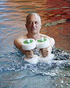 Ein Mann mit zwei Hanteln steht in einem Schwimmbecken.